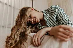 cheerful girl with long curly hair looks down into camera smiles and resting on big comfortable so