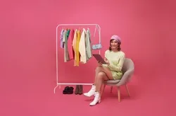 young smiling beautiful asian woman making online shopping and sitting on chair with new clothes